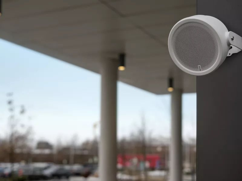 De Axis C1610-VE Netwerk PoE Speaker hangt buiten aan de wand bij een parkeerplaats