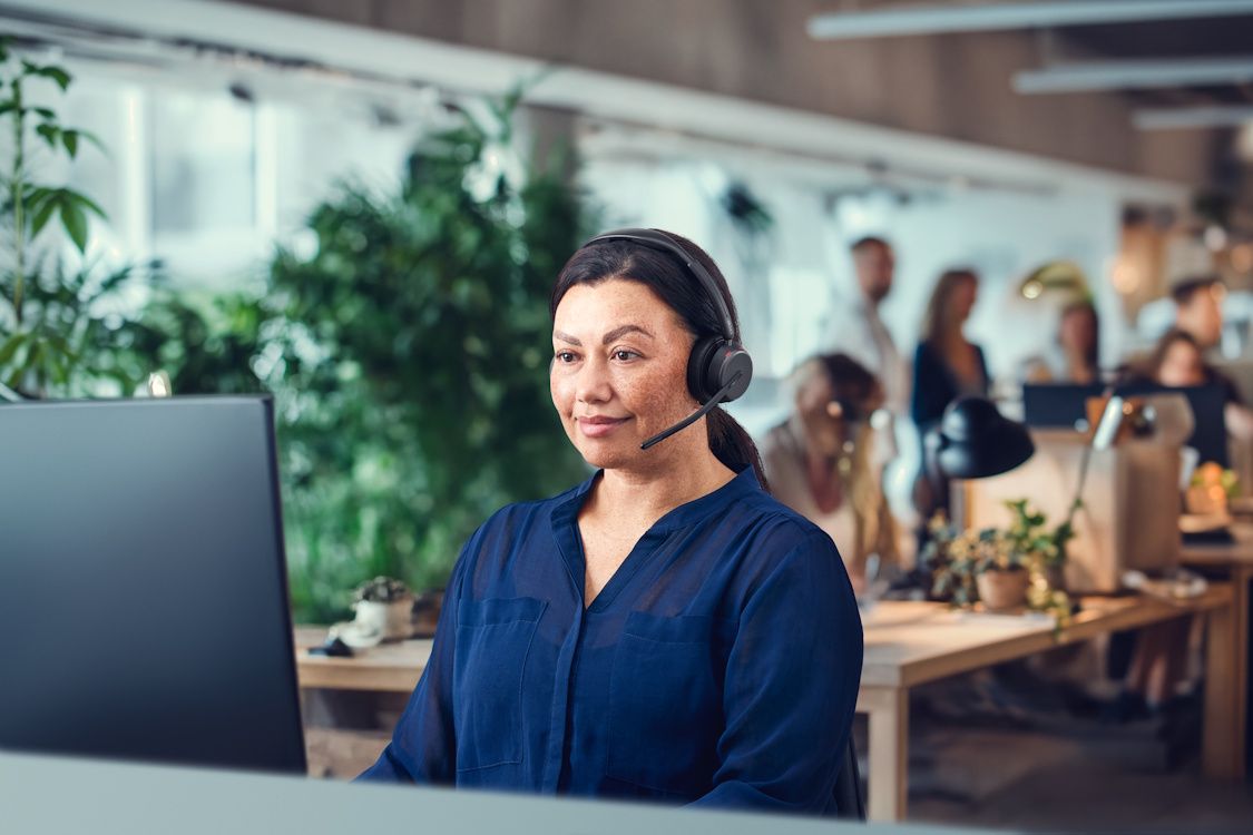 Een vrouw draagt de EPOS IMPACT 1000 MS UC ANC WL dubbeloors Bluetooth headset in een kantoortuin