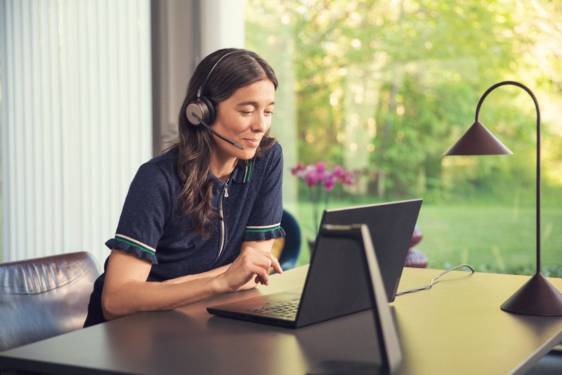 Een vrouw draagt haar EPOS IMPACT 1000 MS UC ANC WL dubbeloors Bluetooth headset op haar thuiswerkplek