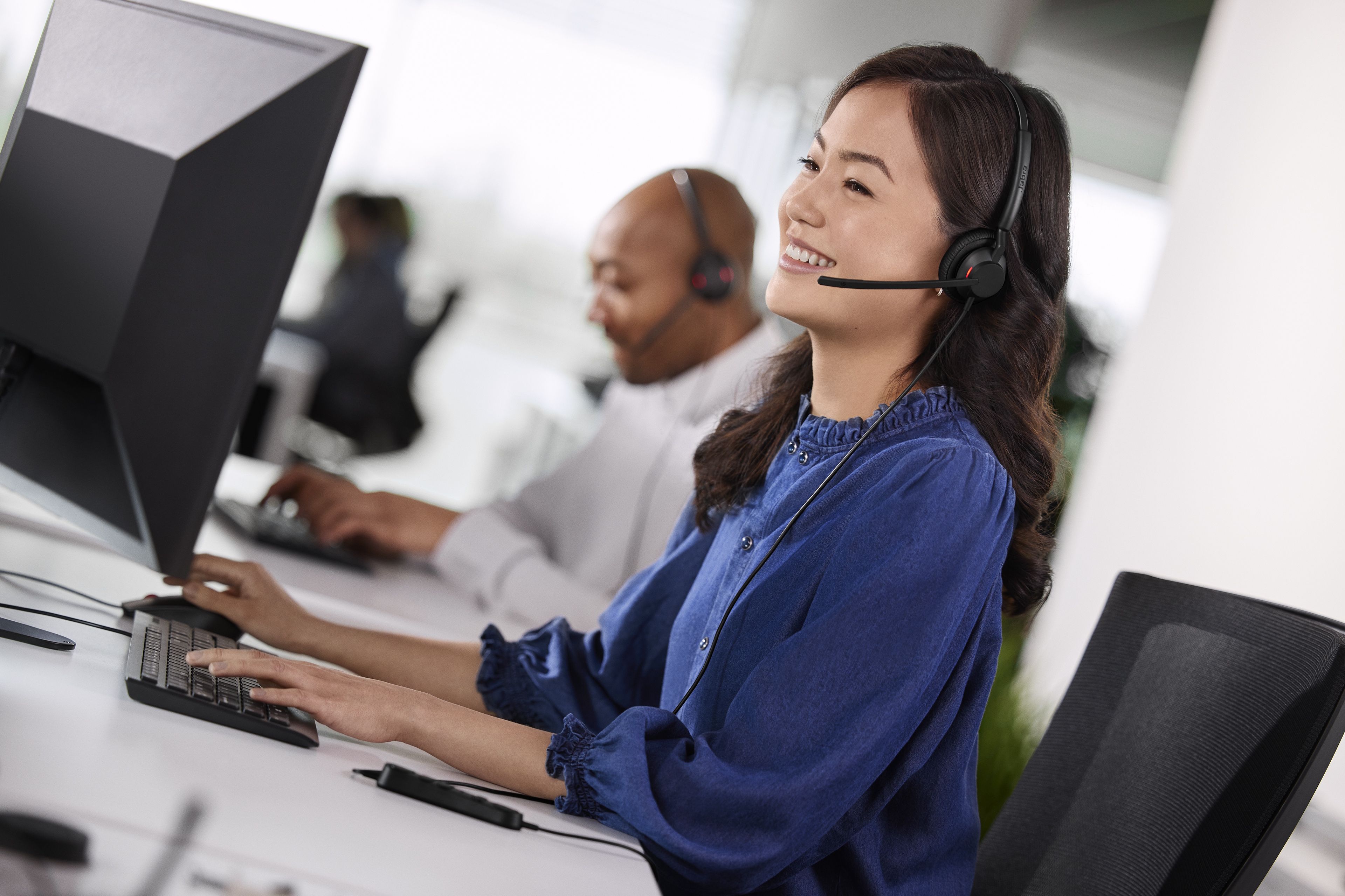 Een vrouw op kantoor met een mannelijke collega ernaast die beiden de Jabra Engage 40 MS Teams stereo USB-C/A headset dragen