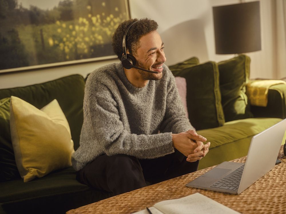 Een man draagt de Jabra Evolve3 45 MS Teams mono Bluetooth headset in zijn thuiskantoor op een groene bank