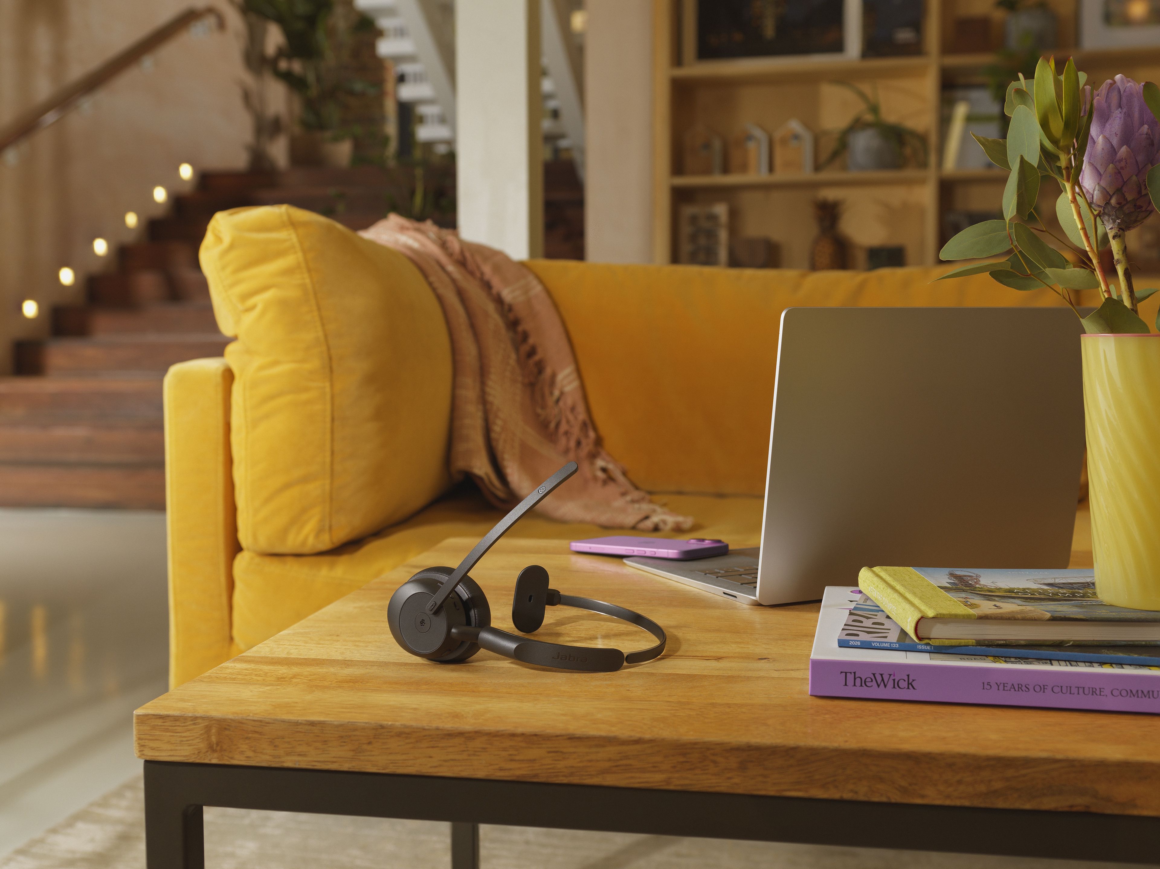 Jabra Evolve3 45 MS Teams mono Bluetooth headset op een tafel met een laptop in een (thuis)kantoor met gele bank