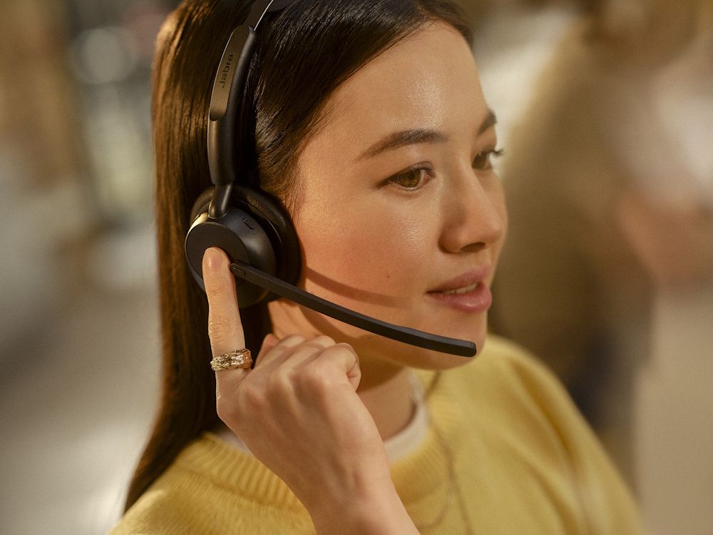 Een vrouw draagt de Jabra Evolve3 45 MS Teams stereo Bluetooth headset en drukt op de Teams knop op het oor