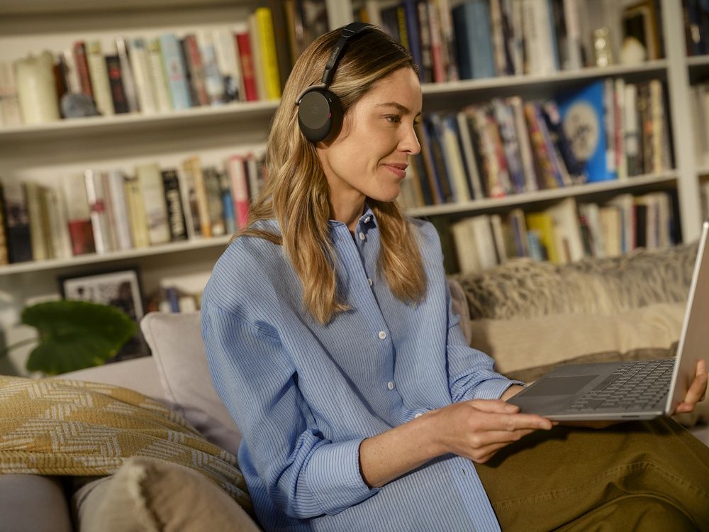 Een vrouw draagt de Jabra Evolve3 65 Flex MS Teams Bluetooth headset op de bank terwijl zij hybride thuiswerkt
