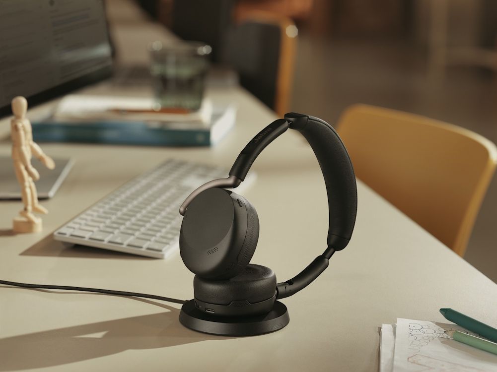 De Jabra Evolve3 65 Flex UC Bluetooth headset op het oplaadstation voor draadloos laden op een kantoorwerkplek