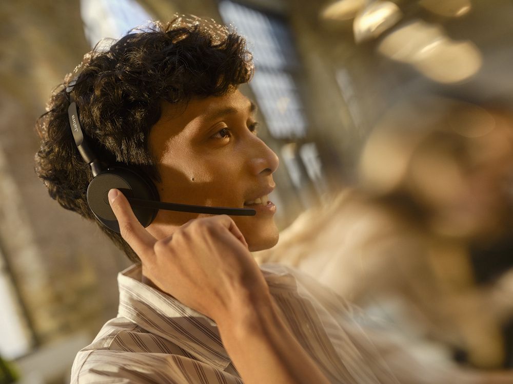 Een man draagt de Jabra Evolve3 65 MS mono Bluetooth headset in een druk kantoor