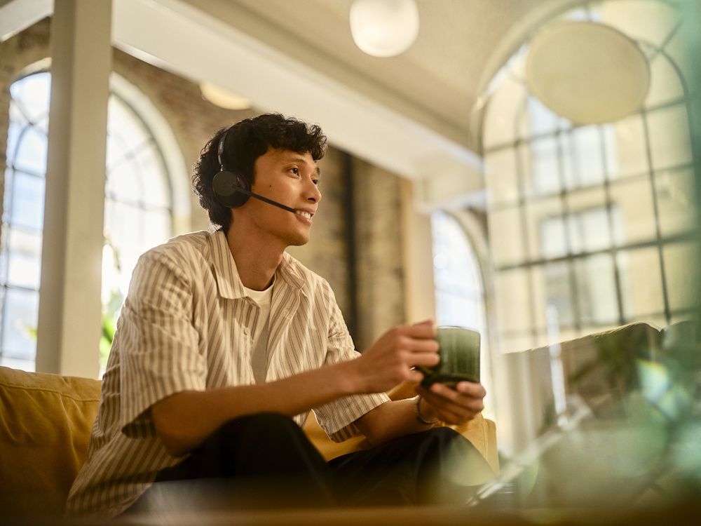 Een man draagt de Jabra Evolve3 65 UC mono Bluetooth headset in een druk kantoor