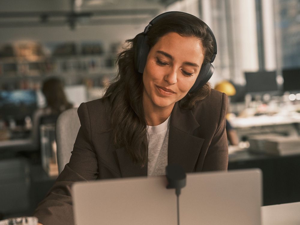 Een zakelijke professional draagt de draadloze Jabra Evolve3 85 UC Bluetooth headset op kantoor achter haar laptop