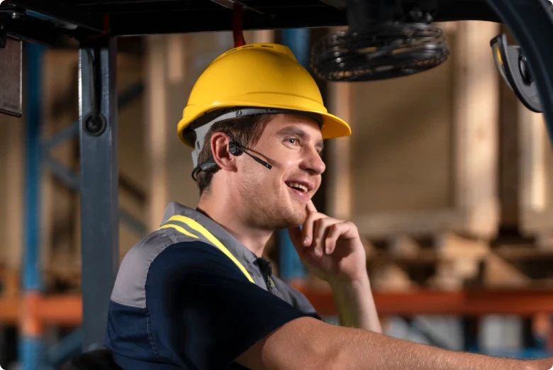 Man met bouwhelm op draag ook de dubbeloors Shokz OpenComm2 bone conduction open-ear headset
