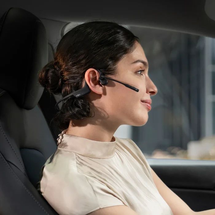 Vrouw in de auto draagt de dubbeloors Shokz OpenComm2 bone conduction open-ear headset achter het stuur
