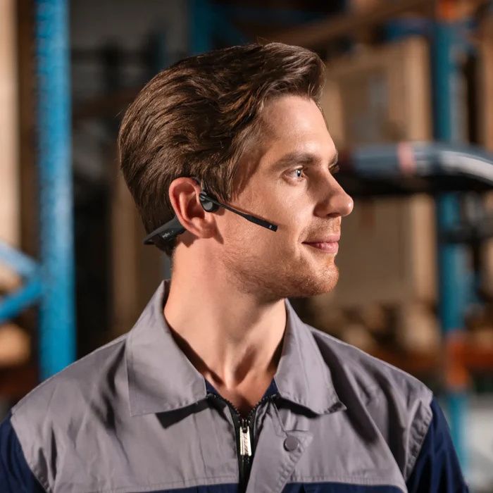Man in een magazijn draagt de dubbeloors Shokz OpenComm2 bone conduction open-ear headset