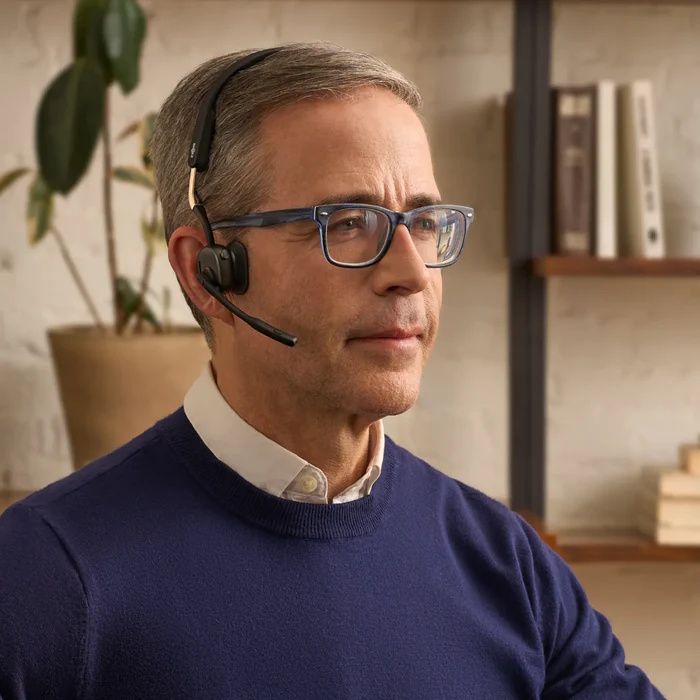 Een man draagt op zijn thuiswerkplek de zakelijke Shokz OpenMeet UC bone conduction en air conduction open-ear headset