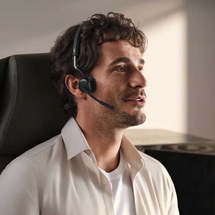 Een man op een bureaustoel draagt de Shokz OpenMeet UC bone conduction en air conduction open-ear headset