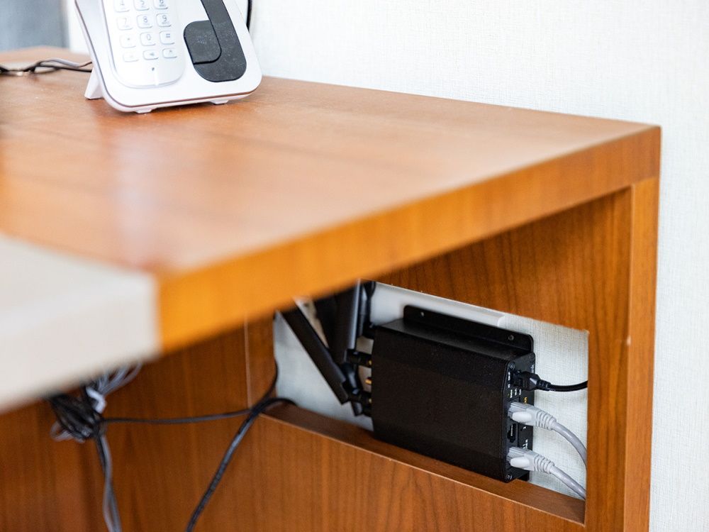 Sfeerfoto van de Peplink MAX BR1 Mini LTE (HW3) 4G LTE router gemonteerd aan de muur en weggewerkt onder een bureau