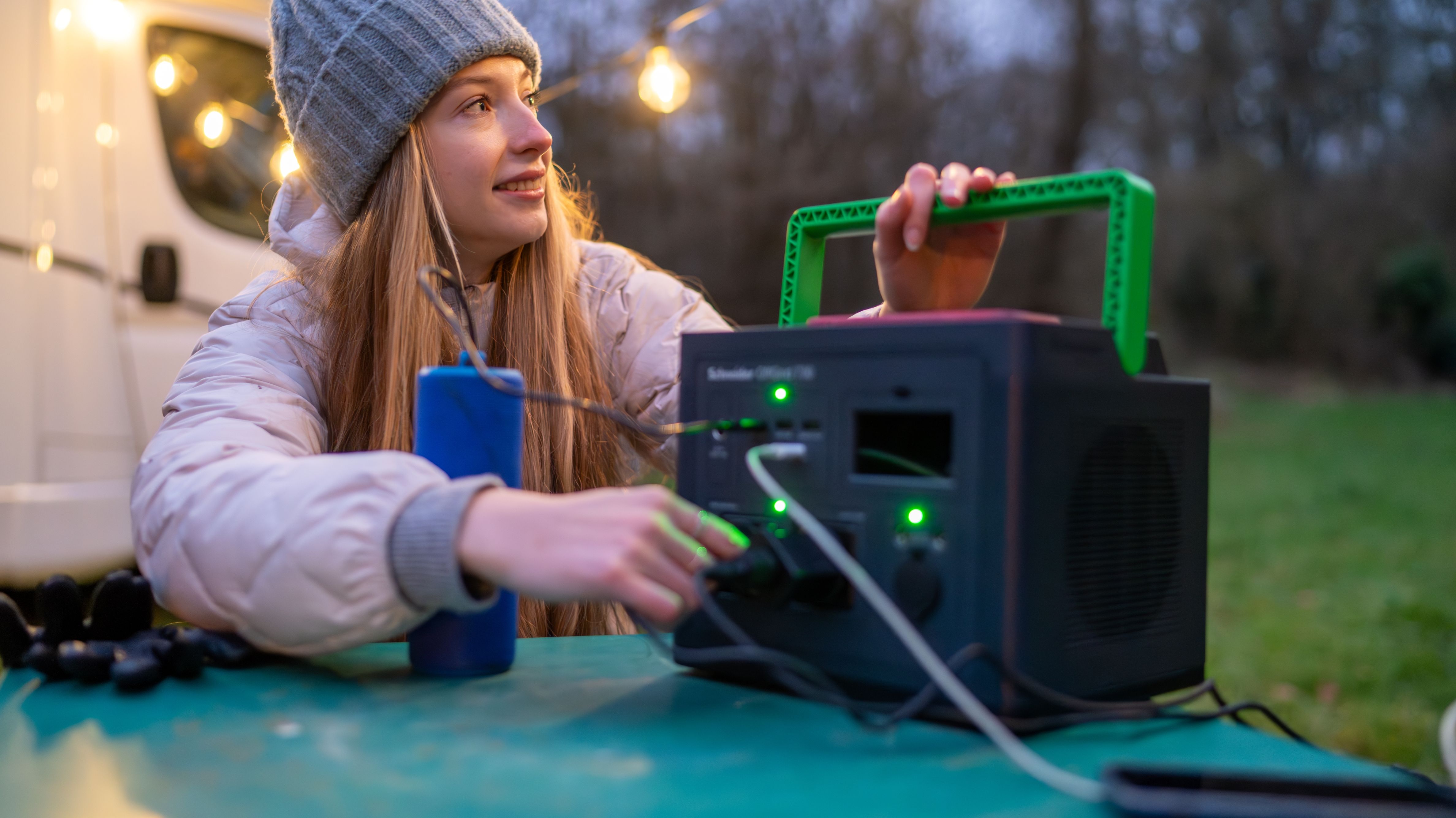 Het APC PPS730-GR draagbare oplaadstation staat op een campingtafel voor een camper en een persoon laadt apparaten op