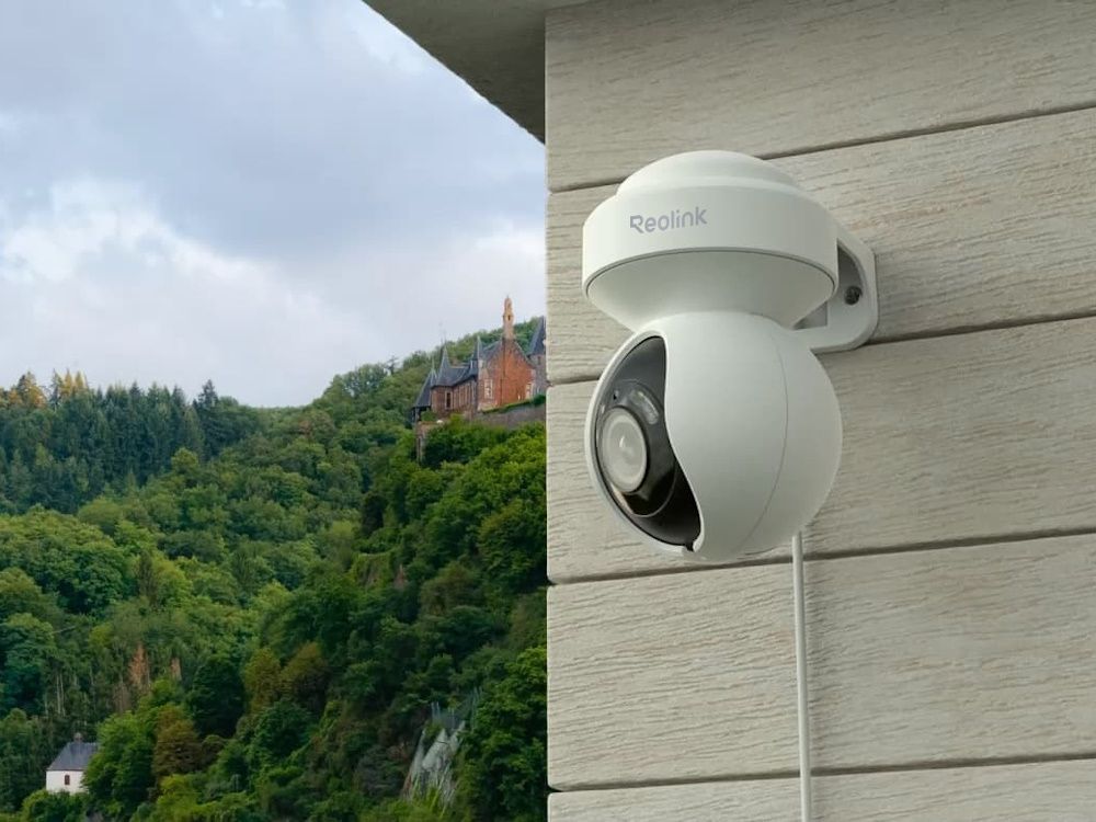 De Reolink E540 outdoor 5MP PTZ WiFi camera wit buiten aan de muur van een woning of bedrijfspand gemonteerd in de groene bergen