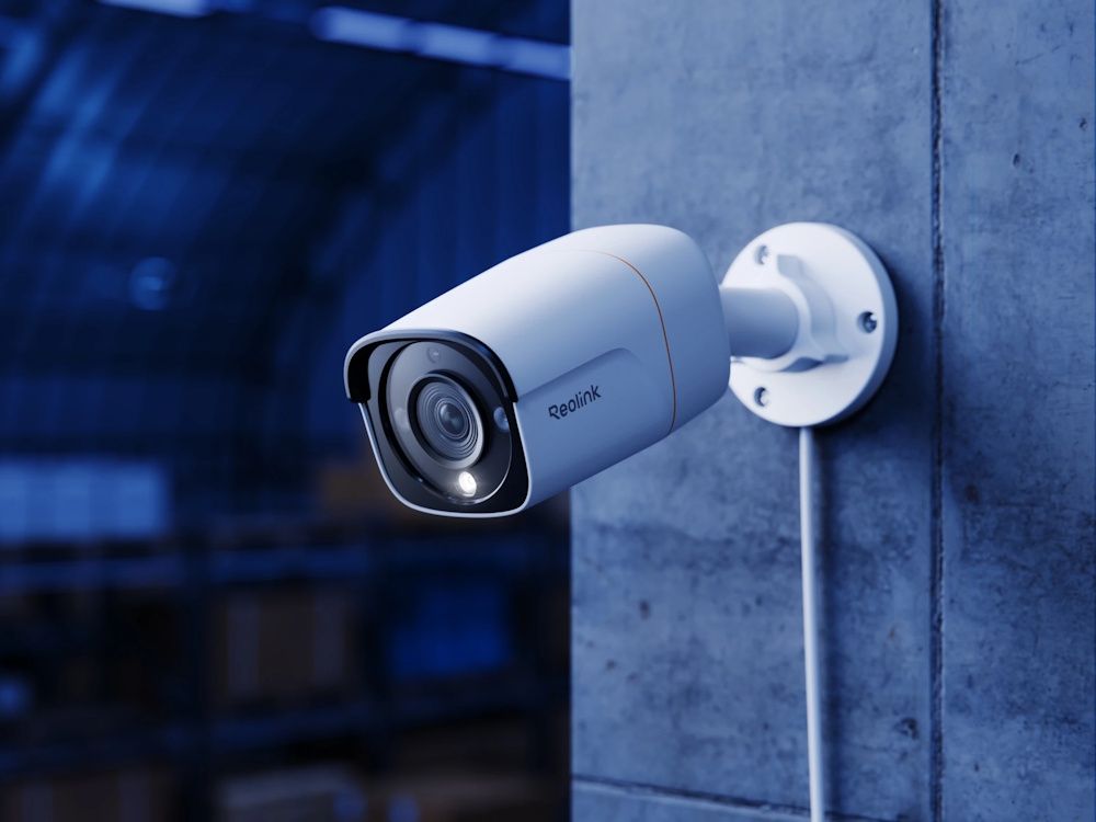 De Reolink Pro RP-PCB12M-W 12MP outdoor PoE camera met spotlights aan een muur geïnstalleerd in het donker