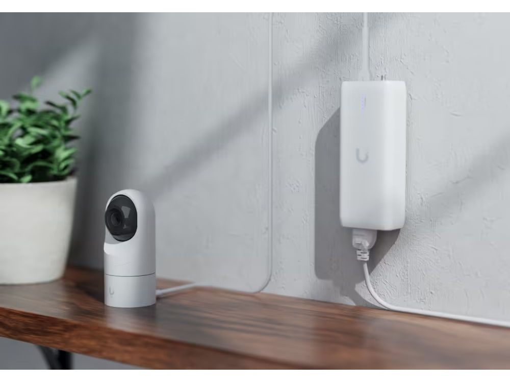 Foto van een thuiskantoor of woning met de Ubiquiti UniFi Device Bridge aan de muur die de aangesloten UniFi Protect IP-camera van Power over Ethernet voorziet